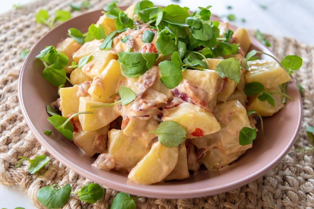 thermomix potato salad in pink bowl with cress on top, on woven placemat