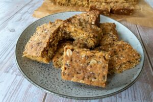 thermomix anzac slice on grey plate, tray of slice in background. on white wood