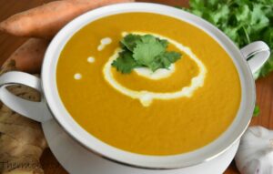 sweet potato soup thermomix made, in white bowl with two handles. Blurred vegetables in background