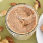 abc nut butter thermomix in jar from top on green tablecloth with nuts scattered around, edge of toast on place on right hand side