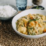 thermomix vegetarian curry in white bowl on straw round placemat with bowl of rice and glass of water in background