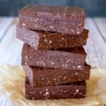 five slices healthy chocolate slice on top of each other, on top of two pieces of baking paper, on wooden table, black background